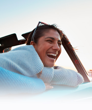 Mujer feliz en el asiento del conductor de un coche, sonriendo con alegría.