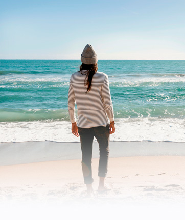 Mujer contemplando el océano desde la orilla de la playa.