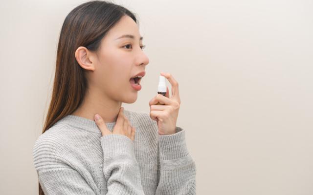 Chica echándose spray porque le salen llagas en la boca.
